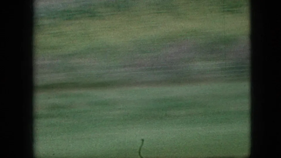 1967 Iowa home-movie frame showing a fast-moving view of green fields with heavy motion blur, grain, and dark 8mm frame edges.