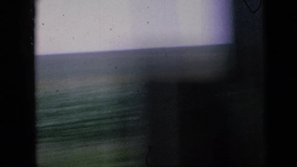 Blurred 1967 Iowa countryside view with green fields, pale sky, and strong film-frame shadow from the moving home-movie camera.