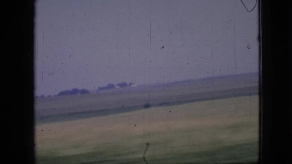 1967 Iowa 8mm frame showing blurred rural farmland and a low horizon from a moving vehicle, with visible film grain and edge marks.