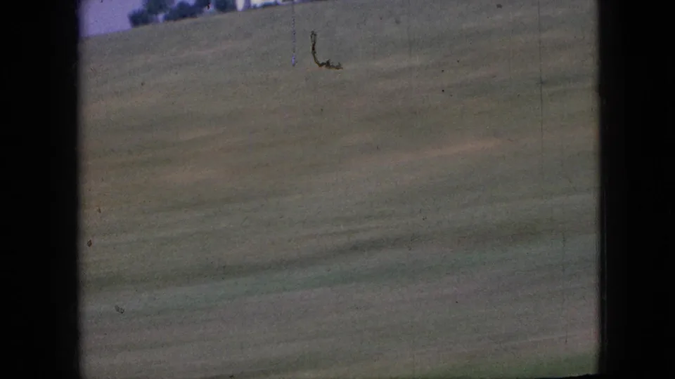 1967 Iowa 8mm frame of a grassy roadside field passing in motion blur, with the vehicle window edge visible along the left and center of the scan.