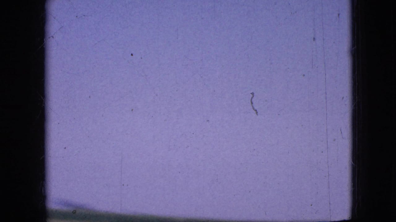 A 1967 Iowa 8mm frame with purple-blue sky and a thin rural horizon line, seen through heavy film gate borders and surface marks.
