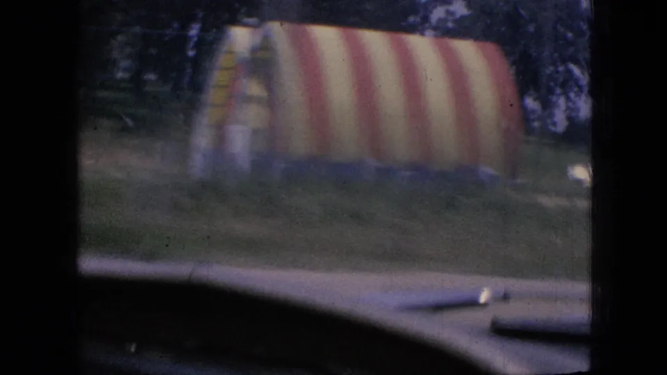 A 1967 Iowa roadside view shows a red-and-white striped tent, possibly at a fair or community event, with the edge of a car hood or windshield area in the foreground.