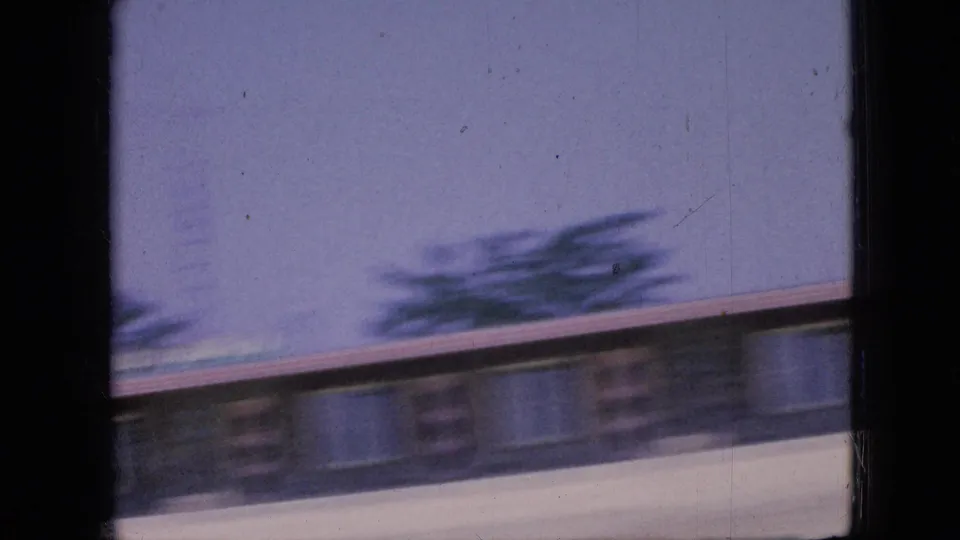 1967 Iowa home-movie frame with a low roadside structure or roofline sliding past under a pale sky, softened by motion blur and 8mm film grain.