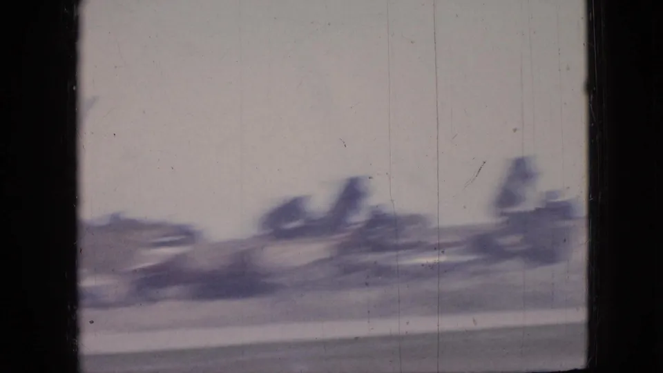 1967 Iowa road-trip frame showing motion-blurred industrial smokestacks or equipment beyond the roadside under a pale sky.