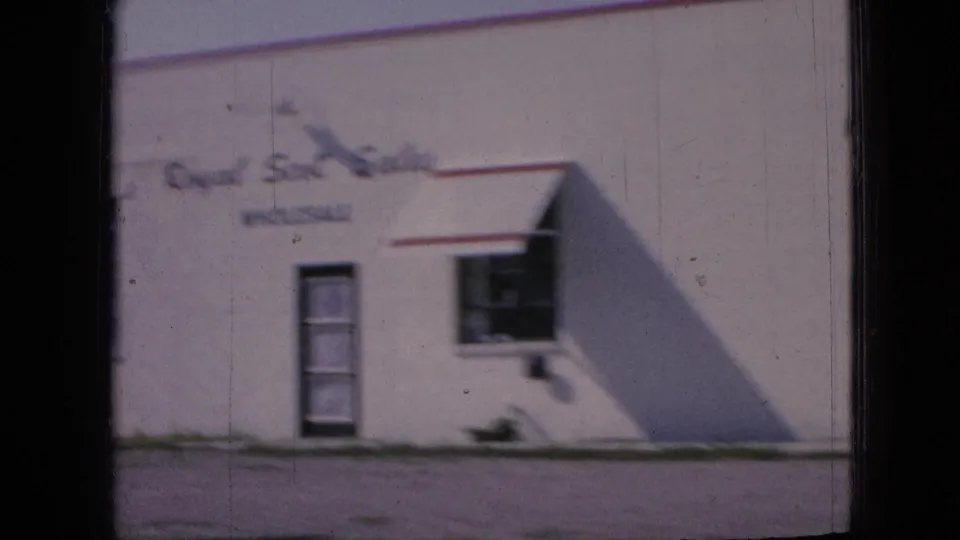 White commercial building in the Iowa footage with red trim, a small window, a door, and partially legible signage on the facade.