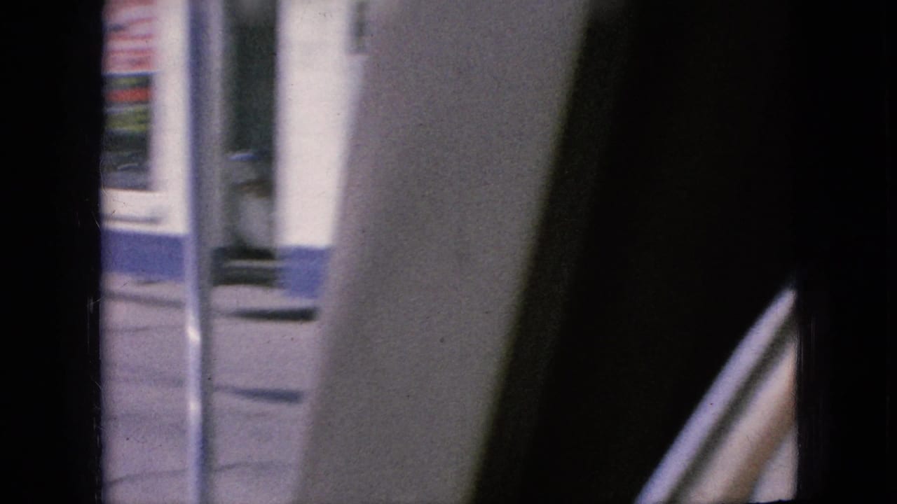 Close view past a car window or pillar with part of a building and a vertical sign blurred in the background.