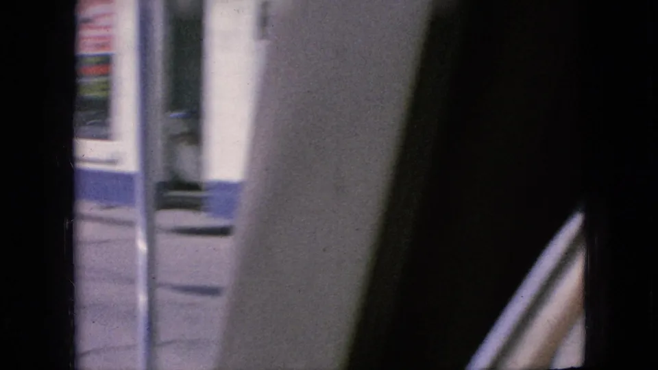Moving 8mm frame from Iowa in 1967 looking past the car interior toward a blurred building facade and partial vertical signage outside.