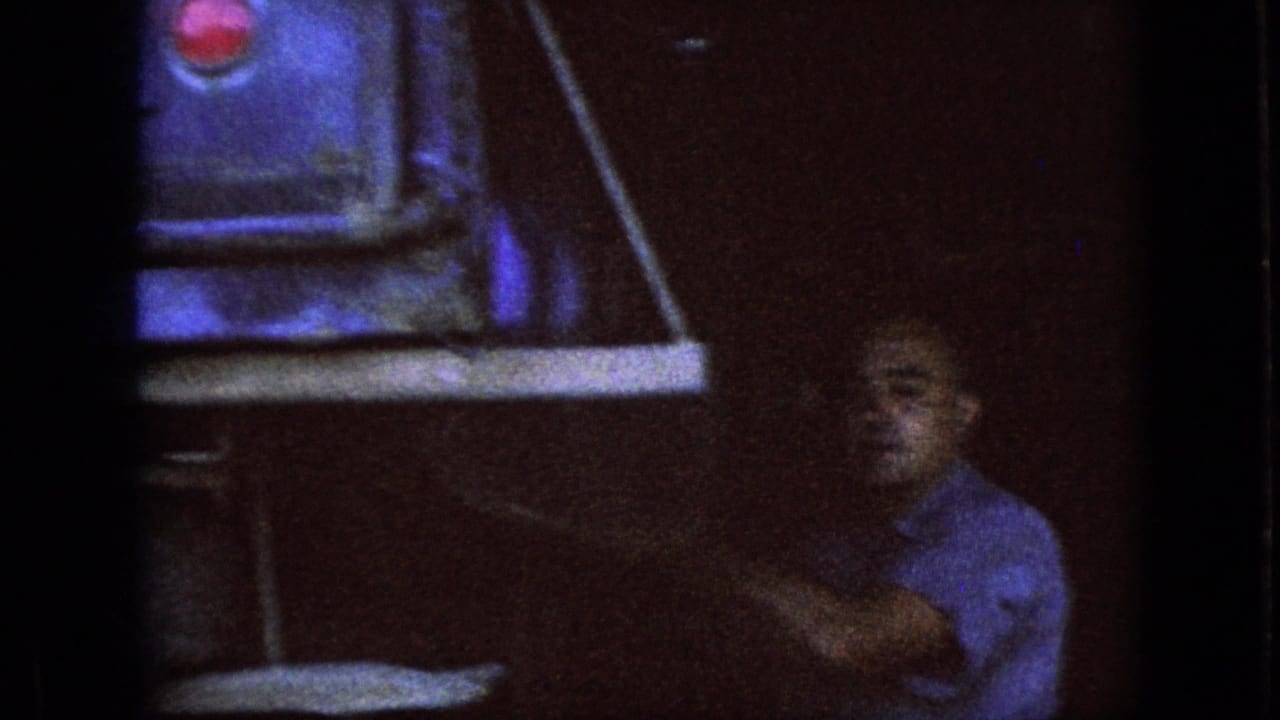 Older man reaches toward a shelf or workbench in a dim garage.