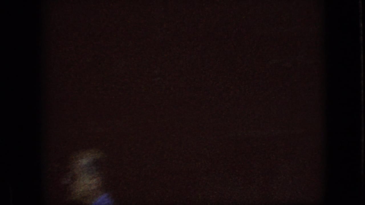 Dark 8mm frame from the 1967 Iowa clip showing an underexposed interior or storefront edge beside a bright, partly blown-out exterior opening.