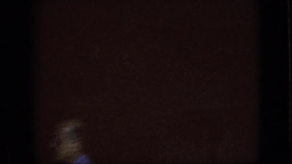 Dark 8mm frame from the 1967 Iowa clip showing an underexposed interior or storefront edge beside a bright, partly blown-out exterior opening.