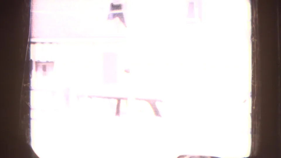 Overexposed daylight frame from the 1967 Iowa home movie with faint building details visible beyond a dark vertical edge.
