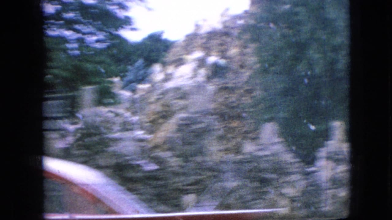 In this 1967 Iowa 8mm home-movie frame, roadside trees and the edge of a red vehicle appear blurred from a moving family car.