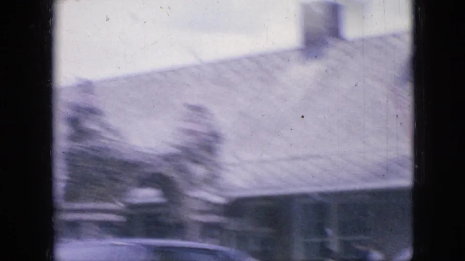 A 1967 Iowa home-movie frame appears to show a cemetery with stone monuments and trees, softened by motion blur and overexposure.