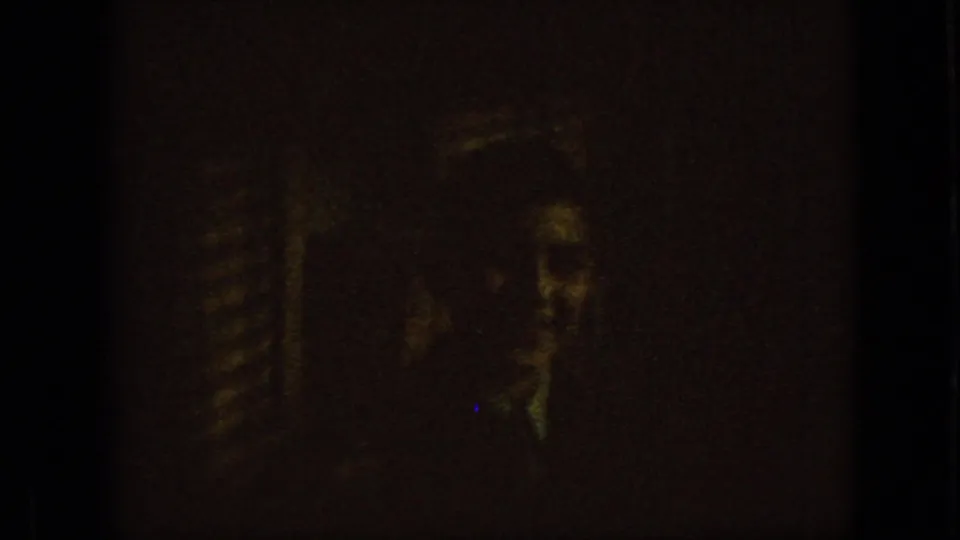 A very dark 1967 Iowa 8mm frame contains a faint, low-light face or figure, with only partial facial features visible through heavy grain.
