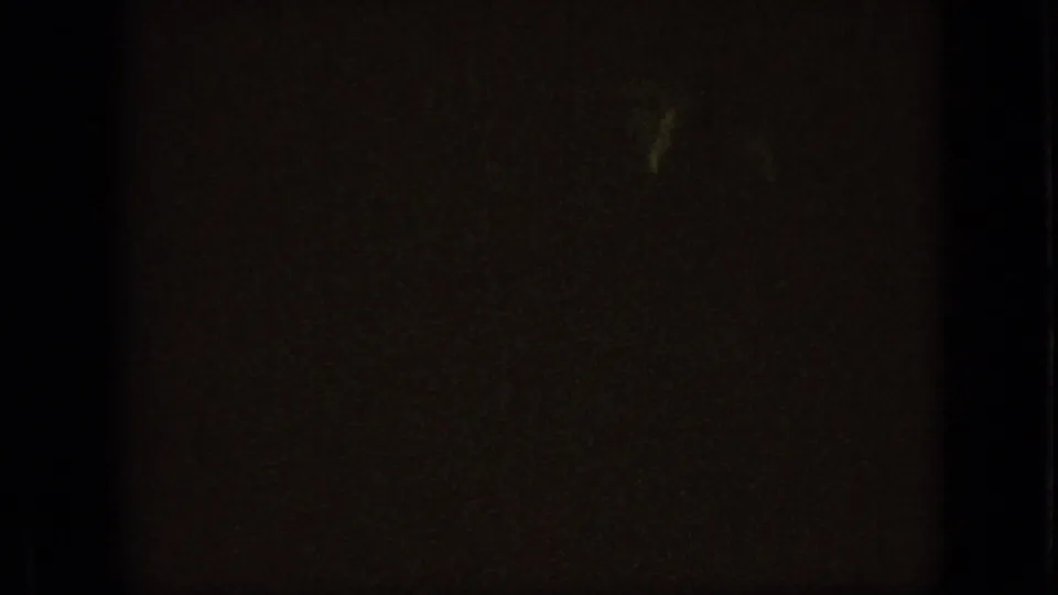 The final 1967 Iowa 8mm frame is mostly underexposed, with a faint yellow-green glow and indistinct shapes suggesting a dark interior or nighttime moment.