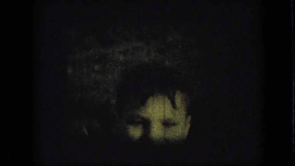 Underexposed 1967 Iowa 8mm frame with a small black puppy barely visible against a dark yard area and film border.
