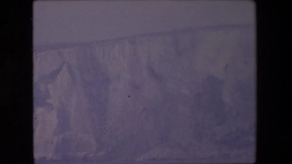 1967 8mm home-movie frame showing a muted, purple-cast view of a snow- or ice-covered mountain slope, with soft focus and visible film gate edges.