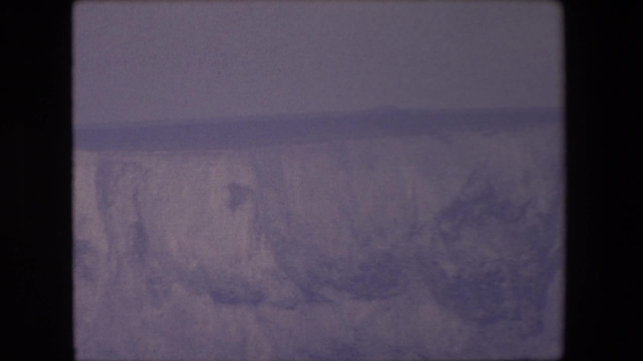 Soft purple frame showing rugged snowy mountain terrain and a dark film edge.