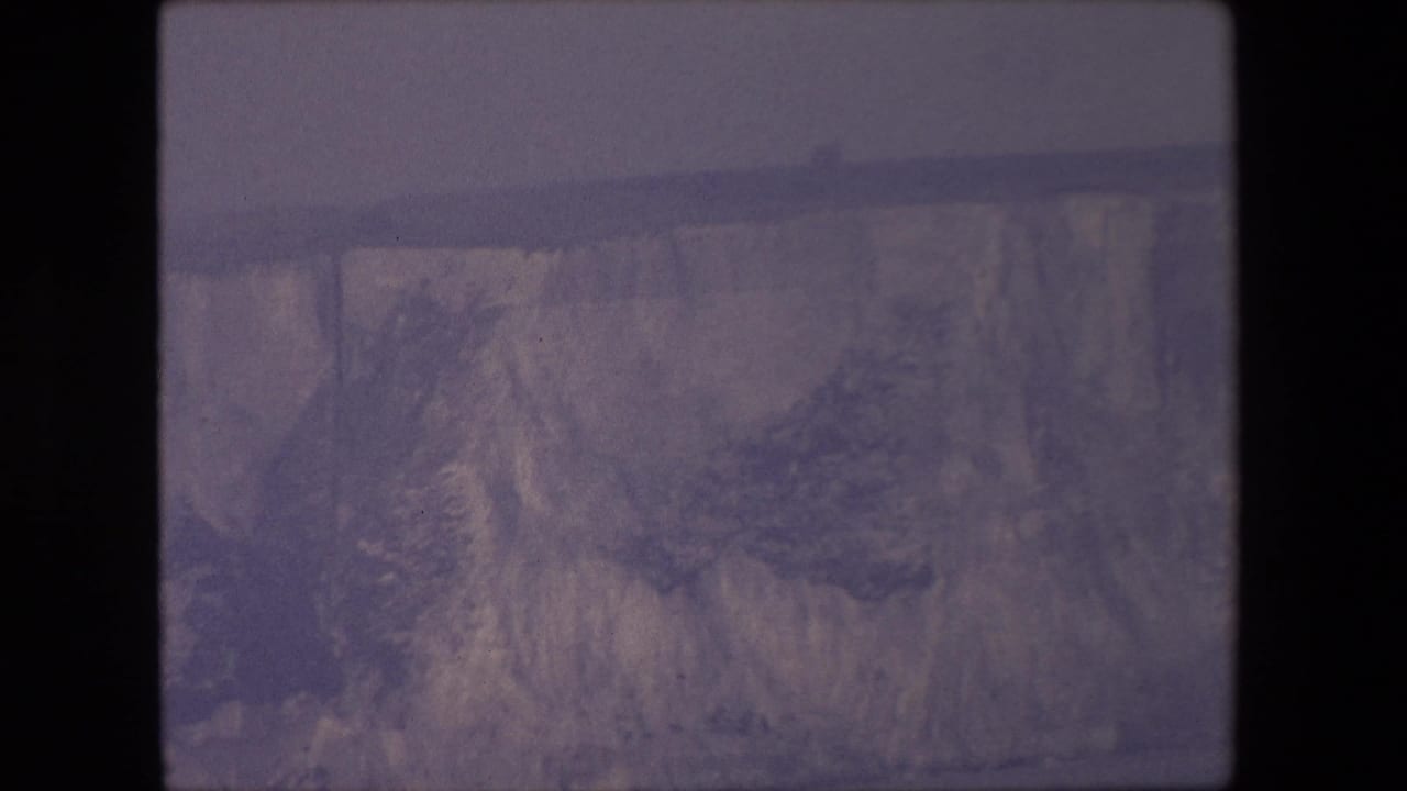 Distant canyon cliff face under a hazy sky with dark film borders.