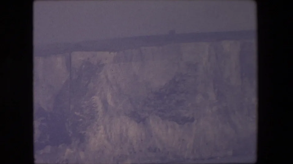 1967 8mm home-movie frame showing a distant canyon wall, pale rock face, and hazy overcast sky within rounded film-frame edges.