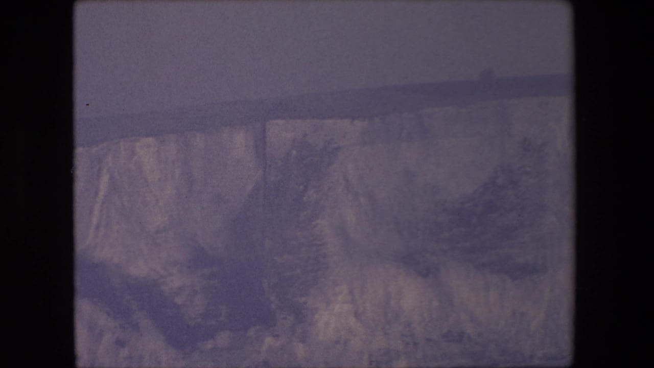 Broad cliff face and canyon rim seen through a soft, purple-tinted frame.