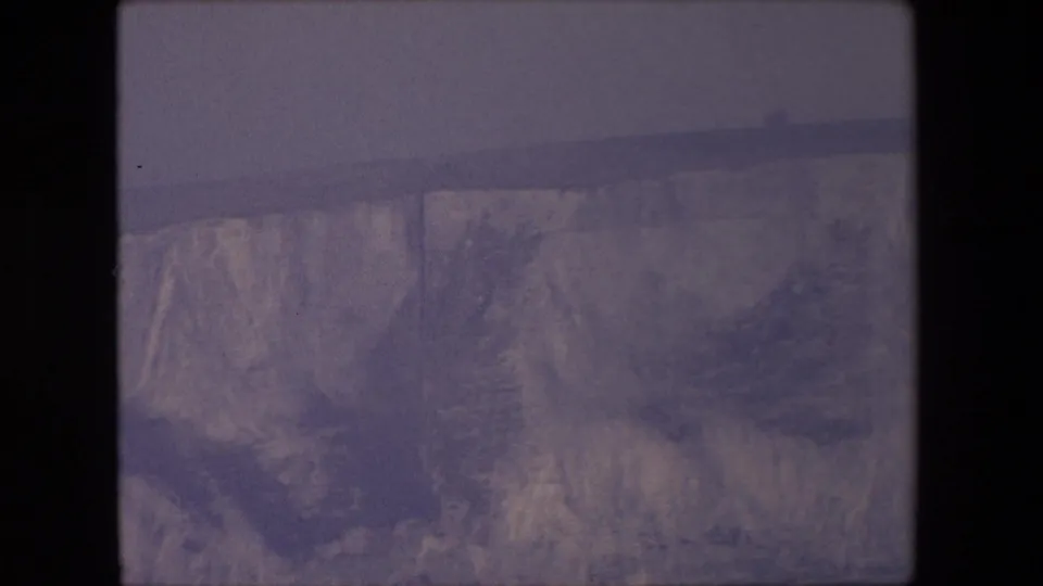 1967 8mm home-movie view of a broad canyon rim and vertical rock face, with muted purple color and slight handheld softness.