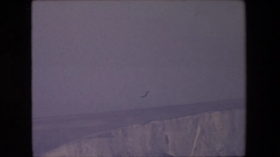 1967 8mm home-movie frame showing a canyon edge along the lower portion of the view, with a wide hazy sky and visible film speckling.