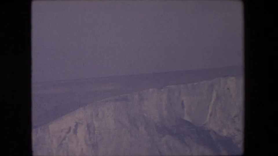 1967 8mm home-movie frame from supplied London, England metadata showing a distant pale cliff face, muted sea, and overcast sky.