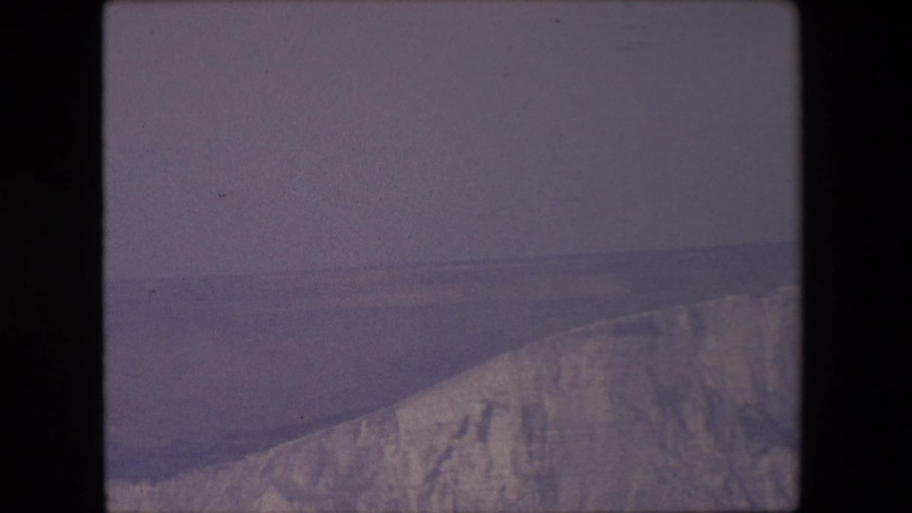 Weathered cliff ridge seen across calm blue-gray water.