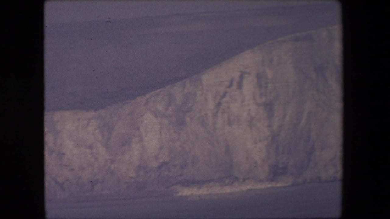 Long chalk cliff face seen across water with waves breaking near the shore.