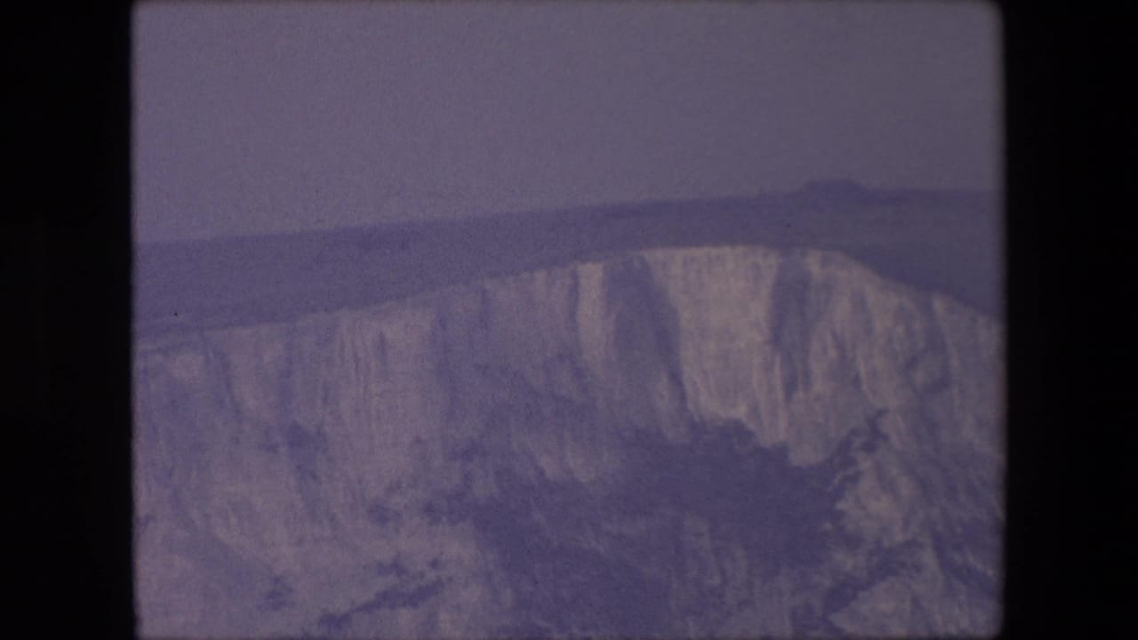 Wide cliff face with a hazy sky and distant horizontal land or sea line.