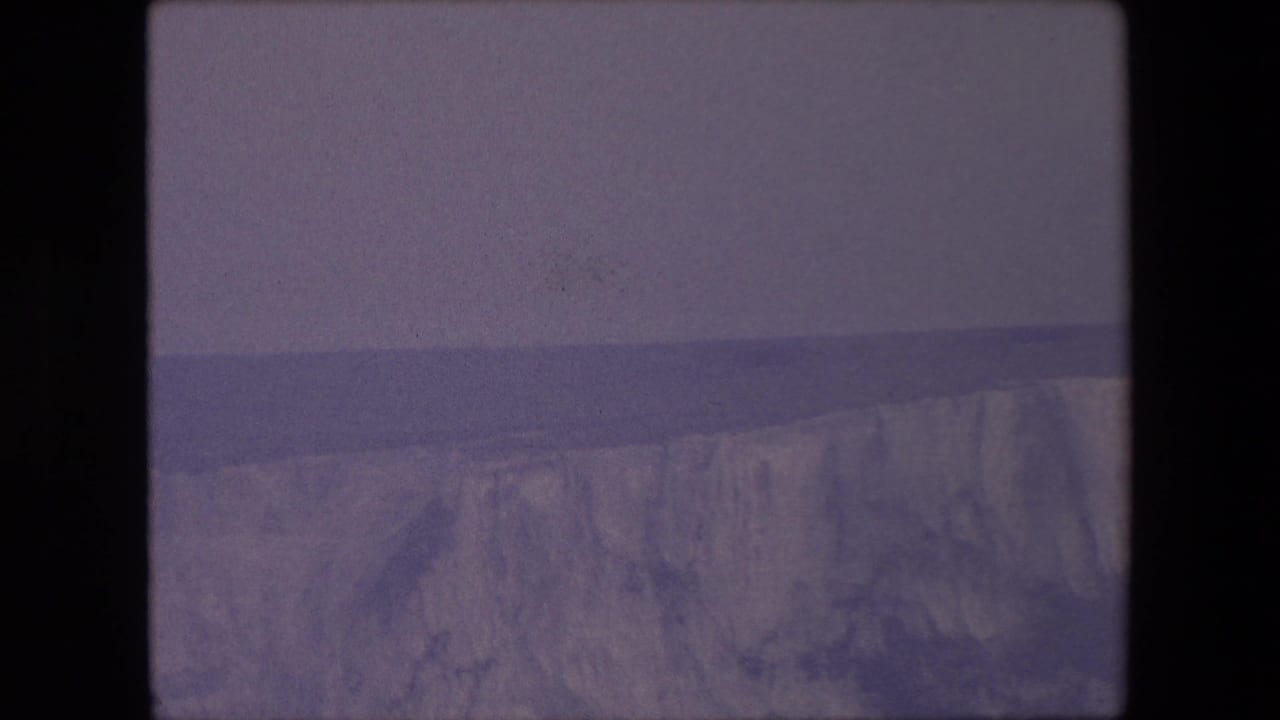 Pale coastal cliffs and sea seen through a faded 8mm frame.