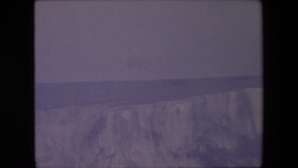 Faded 8mm frame from the stated 1967 England clip showing pale sea cliffs, dark water, and a hazy horizon with no people or buildings visible.