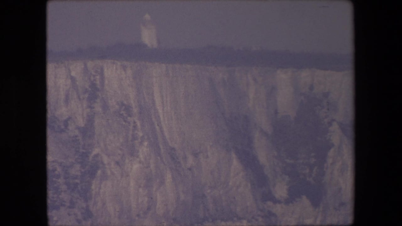 Pale cliff face beneath a gray sky with dark film borders.