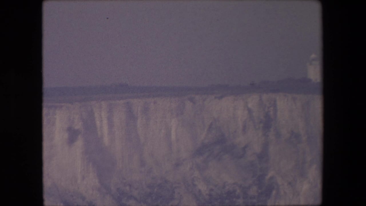 Wide cliff top and pale cliff face with a small distant tower-like structure.