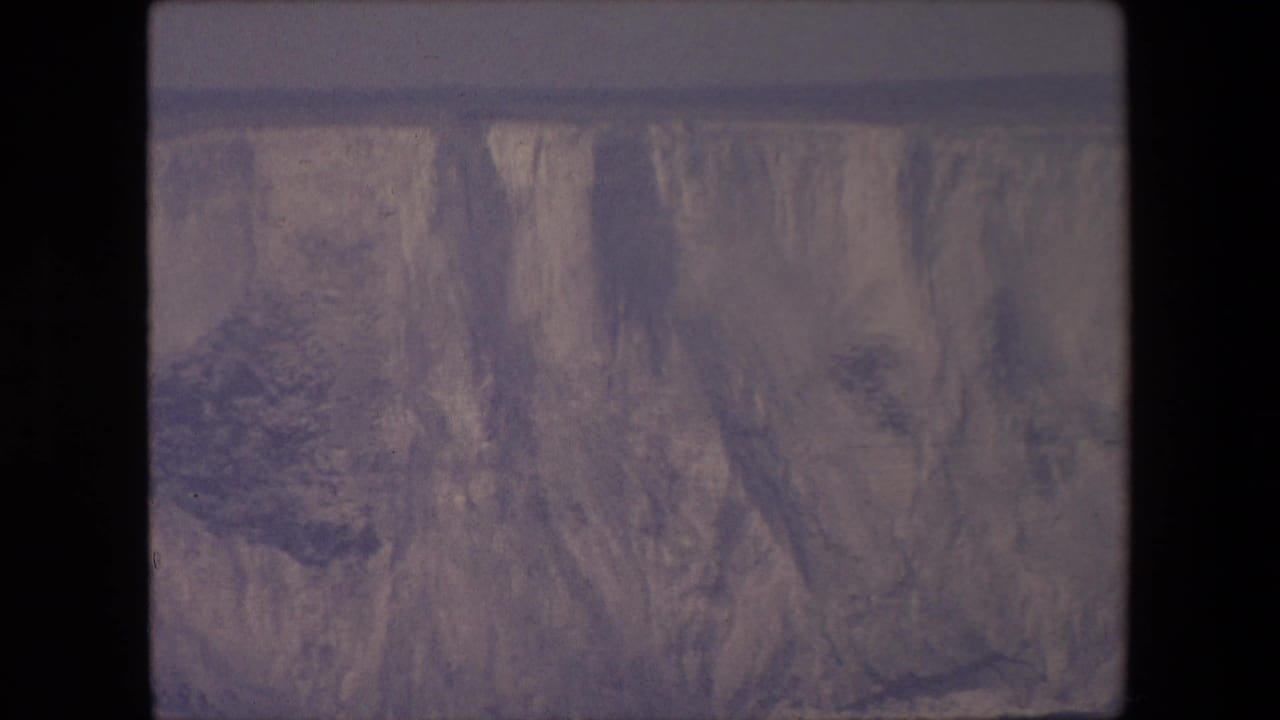 Steep eroded rock face with dark vegetation and muted gray-purple film tones.