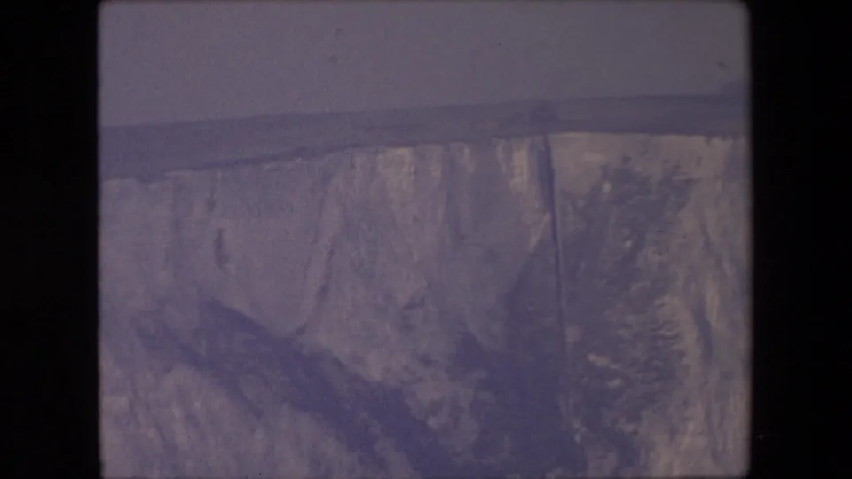 Metadata-supported 1967 London 8mm frame showing a weathered rock face with a darker diagonal form and sparse vegetation at the side.