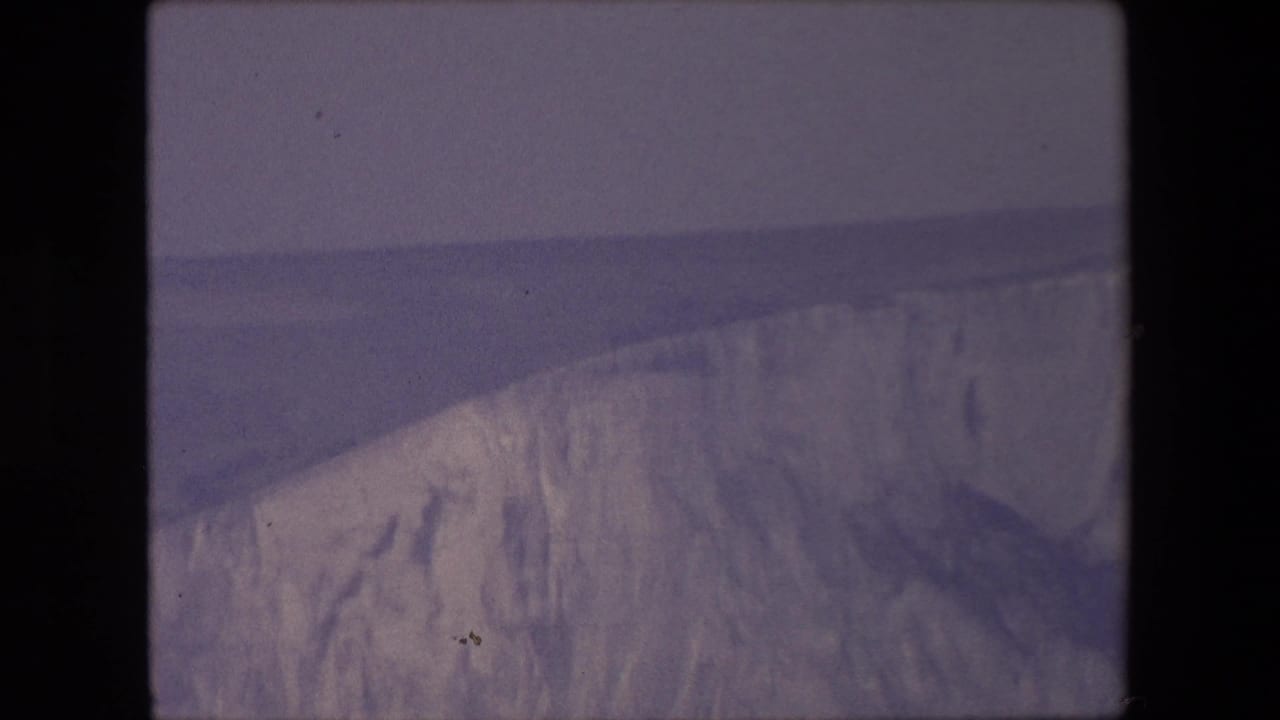 Sloping glacier front with shadowed ice and water below.