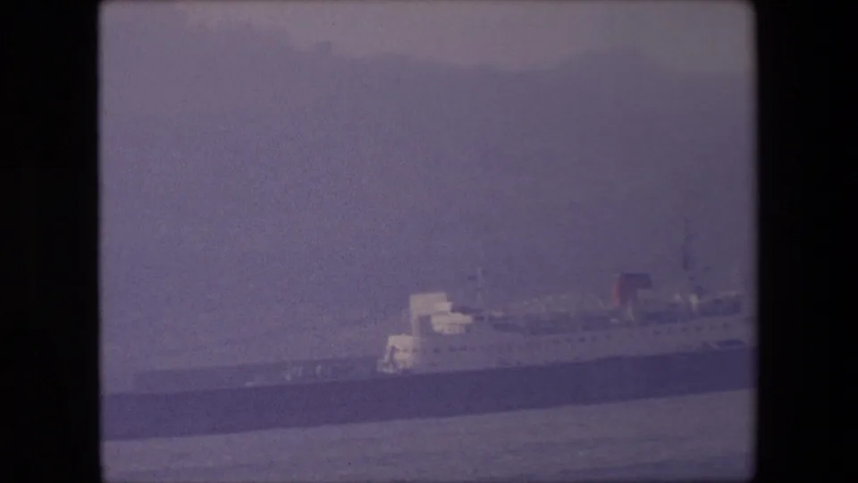 1967 London harbor frame with a large docked passenger ship partly softened by haze, showing its dark hull, pale superstructure, and red funnel.