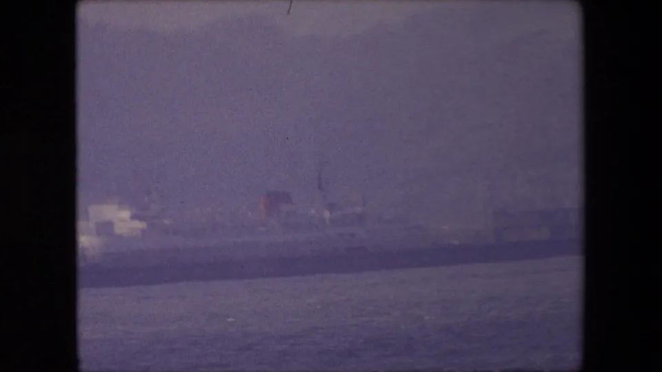 Final 1967 London 8mm frame showing the passenger ship dimly through haze, with its red funnel and dark hull visible above calm harbor water.