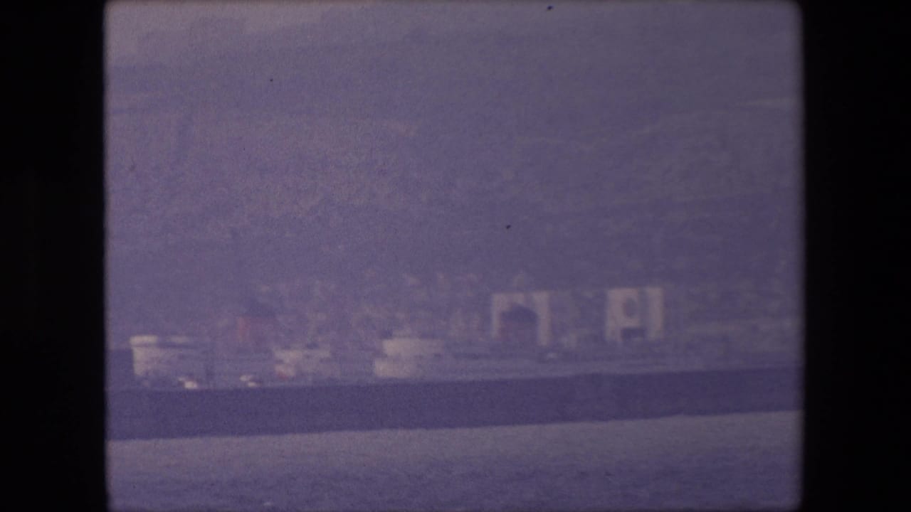 Distant shoreline and pale cliffs across dark water, seen through a soft film frame.