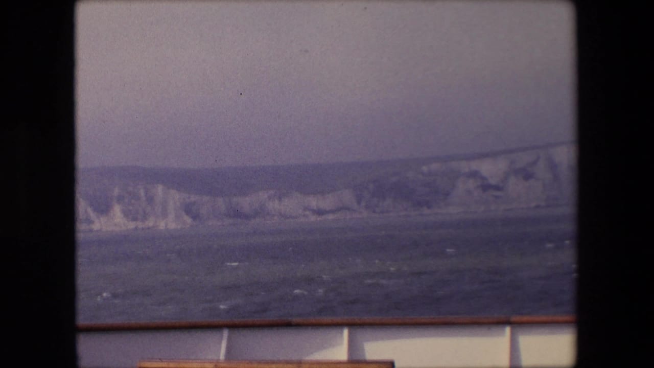White cliff coastline beyond choppy water with a boat rail along the lower frame.