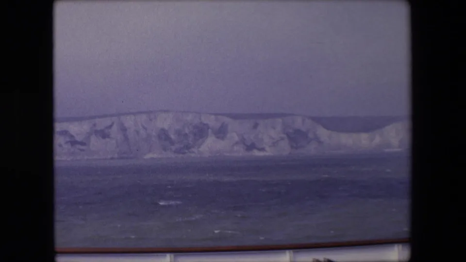 A wider-looking 8mm frame holds on the long chalky cliff line, with open water below and the boat's railing along the lower edge.
