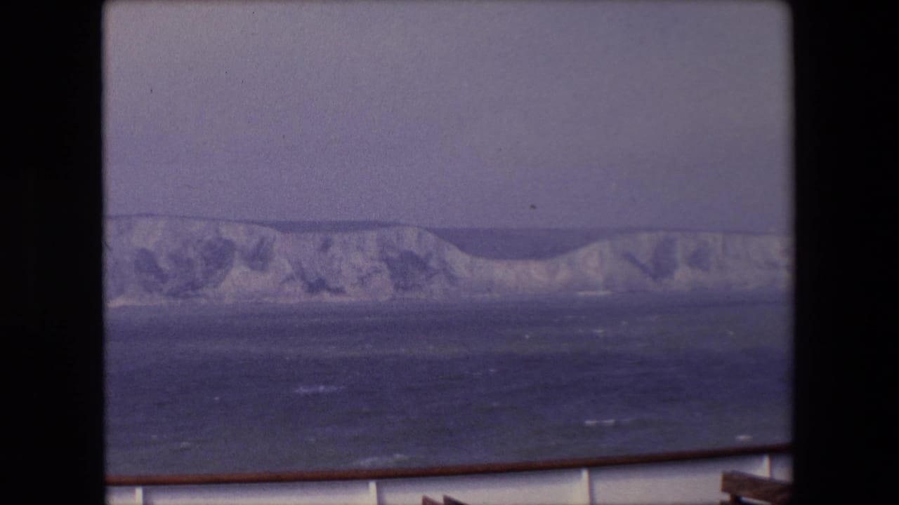 Chalk cliffs seen across choppy water from a boat railing.