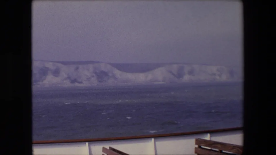 A soft 8mm frame of the White Cliffs of Dover area across choppy sea, with the vessel edge and rail entering the lower foreground.