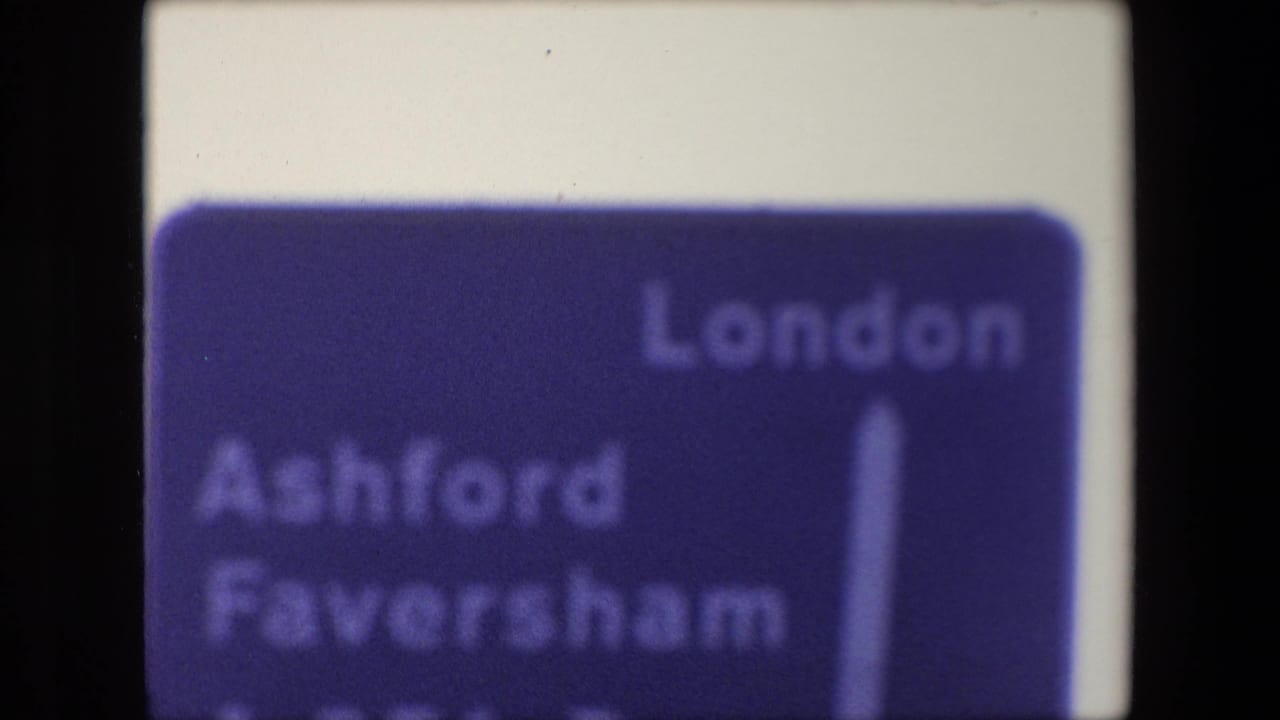 Soft close view of a blue directional road sign with London, Ashford, and Faversham partly visible.