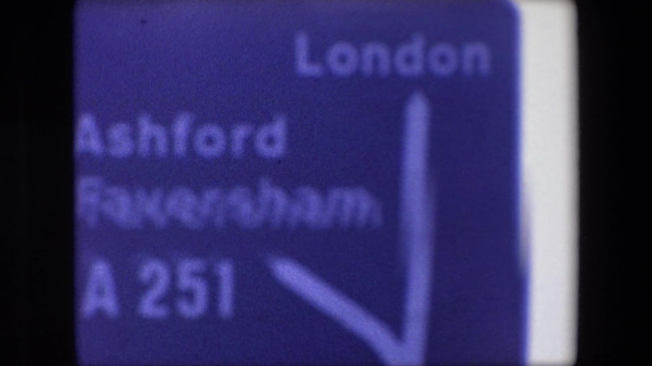 Close-up of a blue road sign showing London, Ashford, Faversham, and A251 lettering.