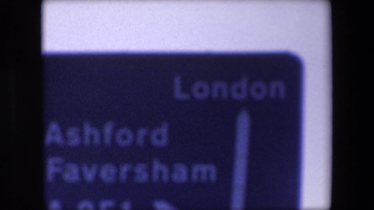 Soft-focus 1967 London travel sign listing London, Ashford, and Faversham, seen with a blue-purple 8mm color cast.