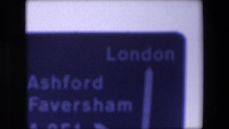 Soft-focus 1967 London travel sign listing London, Ashford, and Faversham, seen with a blue-purple 8mm color cast.