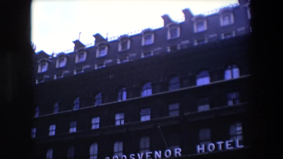 1967 London 8mm frame of the Grosvenor Hotel exterior, showing the roof dormers, upper facade, windows, and bright hotel sign letters near the bottom edge.